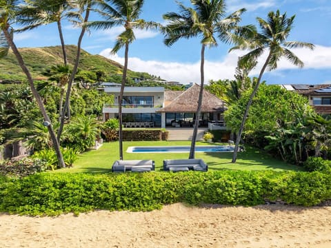 Seen from the sand, the estate spreads across a palm-lined lawn and oceanfront pool.