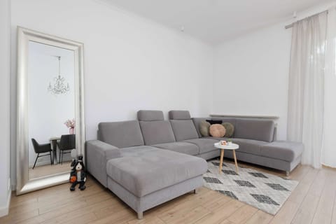 Bright living room with a comfortable corner sofa, coffee table, TV, and large window providing plenty of natural light.