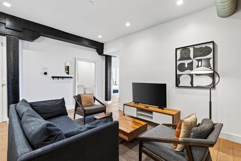 Modern open-concept living area featuring a plush dark sofa, wooden coffee table, and flat-screen TV setup.