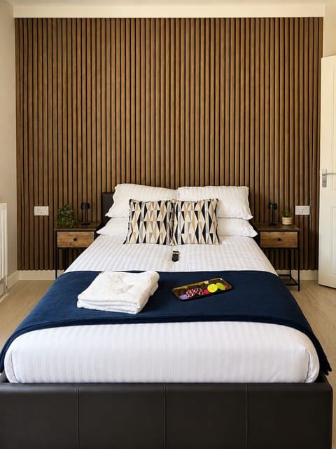 Experience a modern master bedroom featuring a smart TV, wardrobe, complimentary towels, shampoos, shower gel, and a spacious double bed with fresh white linen.
