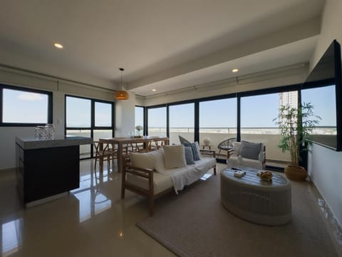 Living area with white cushioned wood sofa, round wood coffee table, and wall-mounted flat screen TV.