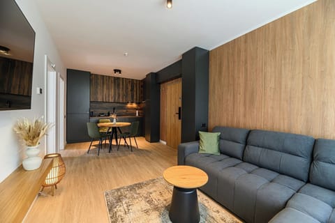 Open-plan living area with large grey sofa, round side table and direct flow into the kitchen and dining zone. Oak wall panelling and light hardwood flooring throughout Grand Chalet Suite 1, Poiana Brasov.
