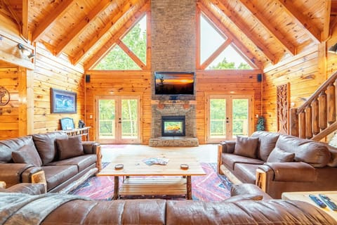 Gather with loved ones in this stunning great room, where vaulted wood-beam ceilings and a towering stone fireplace create a warm, inviting retreat. Natural light pours through floor-to-ceiling windows, framing peaceful forest views.