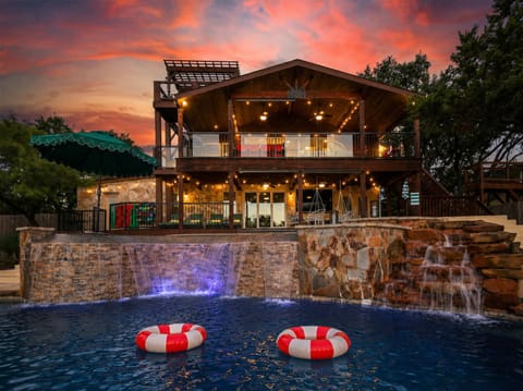Experience magical evenings outdoors with a multi-level deck, illuminated water features, and a glowing custom pool set against a breathtaking sunset sky.