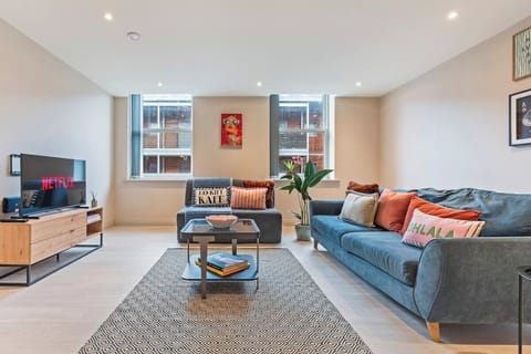 Expansive and light-filled living room featuring a plush blue sofa, modern media console, smart TV, and stylish geometric area rug.