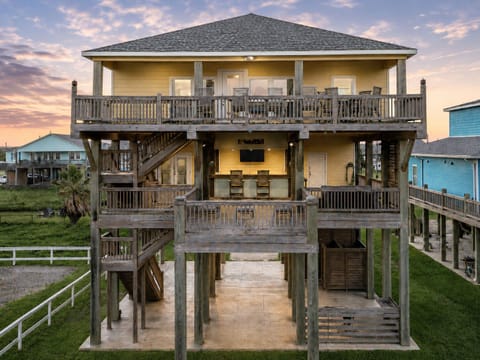 Waves and Whiskey welcomes guests with an elevated beachfront setting beneath a colorful sunset sky. This spacious coastal home offers a memorable escape just steps from the sand and ocean.