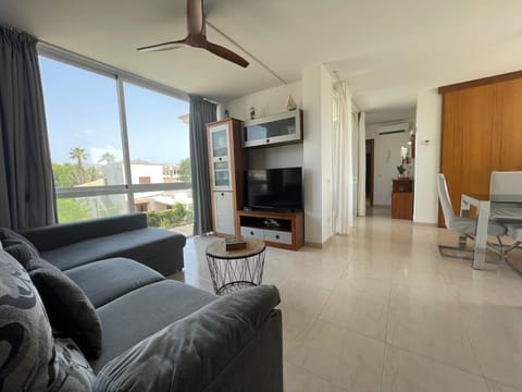 Open-plan living and dining area with large windows, comfortable sofa, Smart TV, integrated dining space and plenty of natural light, creating a bright and welcoming atmosphere.