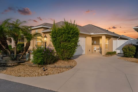 A welcoming single-story home with tropical landscaping and a spacious driveway, set beneath a stunning sunset sky in a peaceful neighborhood.