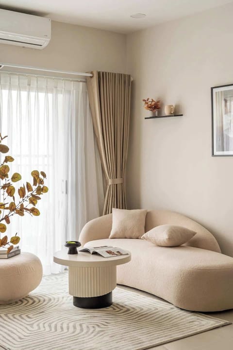 Relax and unwind on the cozy cream lounge with plush cushions, set beside soft natural light and calming decor. The space offers warmth, comfort, and a touch of charm for afternoon reads or morning coffee.