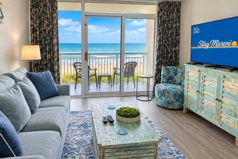 Relax in this beautifully updated oceanfront living room, featuring stylish coastal décor, a large Smart TV, and stunning balcony views of the Atlantic Ocean.