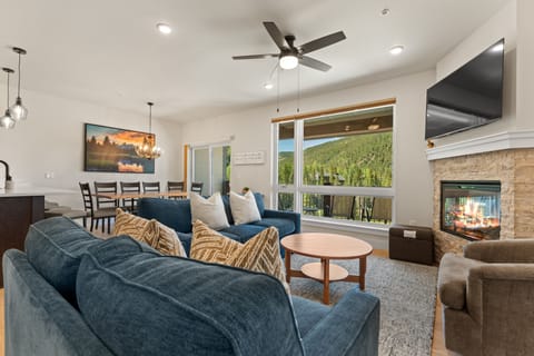 Step into your open-concept living space where plush seating, a crackling fireplace, and stunning mountain views through expansive windows invite you to unwind completely.