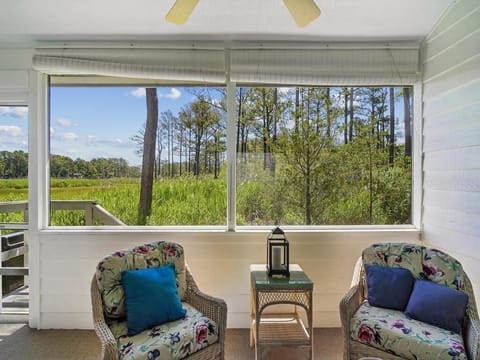 Two wicker chairs with floral cushions on the screened-in porch, overlooking the greenery outside