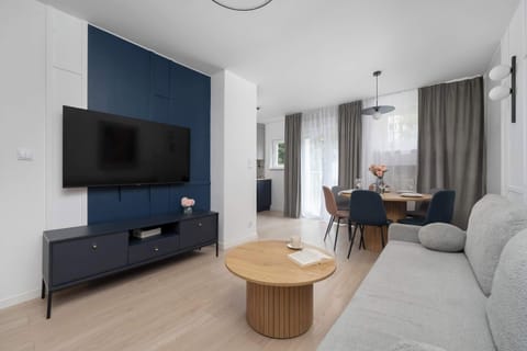 A modern living room featuring a dark blue TV wall and a cozy gray sofa facing a round wooden coffee table. Soft lighting accents the contemporary decor, creating a welcoming atmosphere.