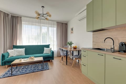Jasny i przytulny salon z wygodną sofą, elegancką strefą wypoczynku i dużymi przeszkleniami zapewniającymi naturalne światło. Turkusowe akcenty, dekoracyjny dywan i harmonijna aranżacja nadają wnętrzu świeży, nowoczesny charakter.