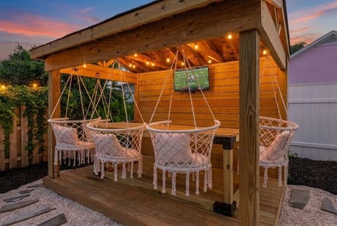 Cozy backyard gazebo with hanging chairs, string lights, and outdoor TV