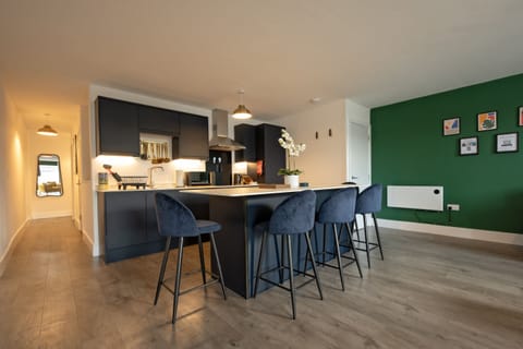 Open-plan kitchen with breakfast bar seating and a green feature wall