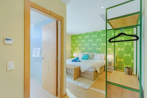 Step into your cheerful bedroom, where vibrant green leaf-patterned walls and warm wood tones create a fresh, inviting atmosphere. You'll find plush towels ready in your private bathroom and convenient storage right at hand.