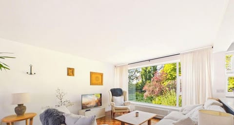 The main sitting room stretches out in soft creams and warm parquet, with a picture window pulling the garden`s colour right into the room.