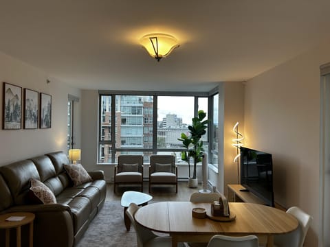 Living room with leather sofa, two armchairs by large windows, modern floor lamp, and wood dining table under ceiling light.