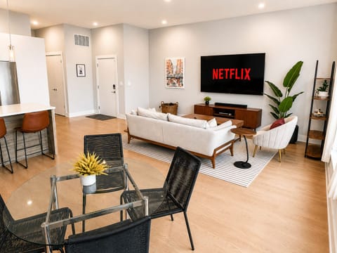 Bright modern living room with large TV, dining space, and stylish decor