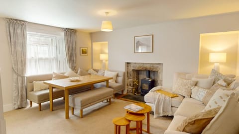 The sitting room with a wood burner in the fireplace and the dining table set under the window. Light comes in from the front of the house.
