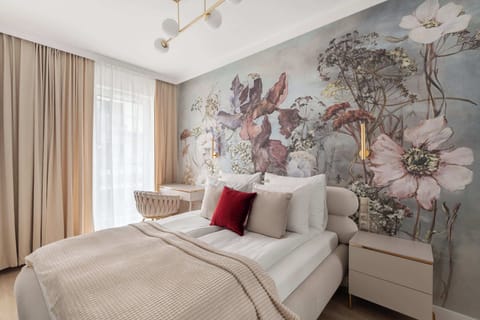 Elegancka sypialnia z efektowną, artystyczną dekoracją ściany, która nadaje wnętrzu wyjątkowego charakteru. Jasna aranżacja, komfortowe łóżko i subtelne detale tworzą przytulną, harmonijną przestrzeń sprzyjającą wypoczynkowi.