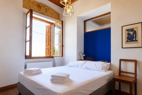 A bright and peaceful bedroom with a comfortable double bed, fresh towels, wooden-framed windows and simple traditional details, creating a relaxed space to rest after a day exploring the coast and surrounding villages