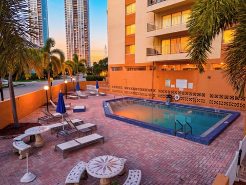 Unwind by the palm-lined community pool at sunset, with lounge seating and high-rise city views creating an urban backdrop.