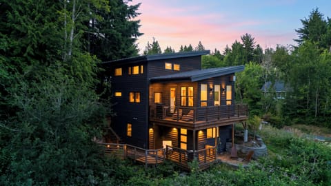 Twilight forest retreat with warm interior lighting, layered decks, and a peaceful wooded setting.