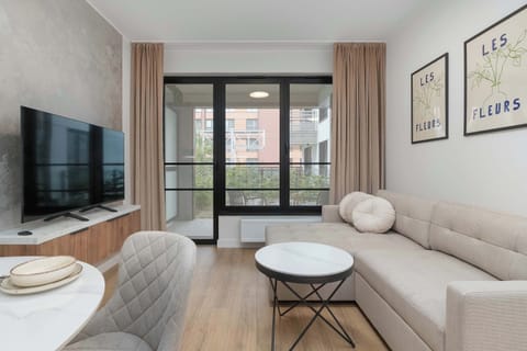 A bright living room with a sofa, TV, coffee table, and large windows.