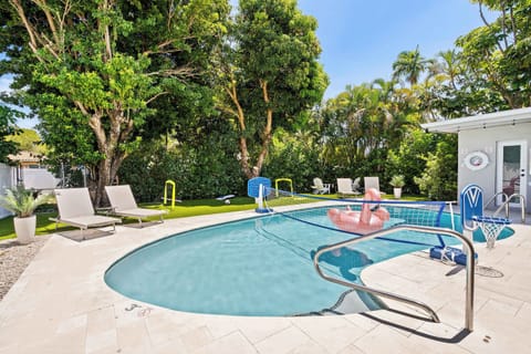 Private swimming pool with patio seating, a outdoor dining area, and a fire pit table set in a green backyard.