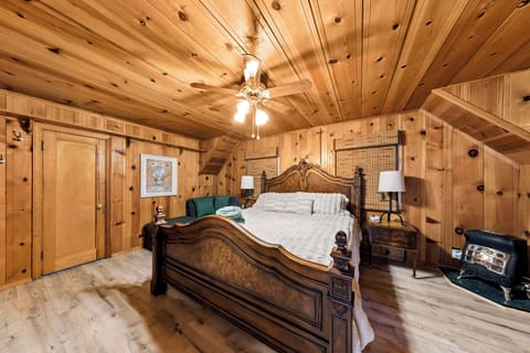 Luxurious primary suite offering a carved wood bed frame, vaulted knotty pine ceilings, ceiling fan, and its own cozy stove heater.
