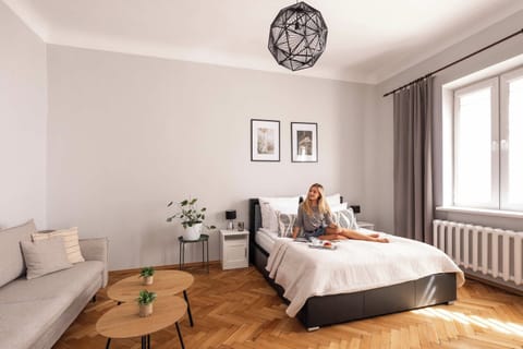 Elegancka i przytulna część mieszkalna z wygodnym łóżkiem, sofą i klasyczną podłogą ułożoną w jodełkę. Duże okna zapewniają naturalne światło, a stonowana kolorystyka, stylowe oświetlenie i subtelne dodatki tworzą harmonijną przestrzeń do wypoczynku.