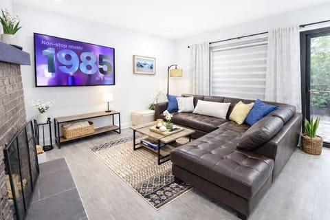 Unwind in the spacious, sun-drenched living area featuring an oversized tufted leather sectional, a massive wall-mounted Smart TV for all your streaming needs, and custom window treatments that allow you to easily transition from a bright, airy works