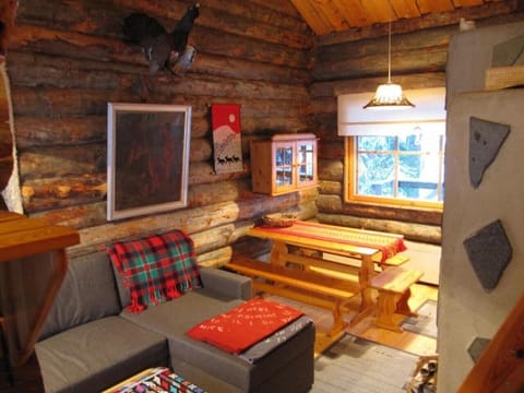 Cosy log-walled living room with a sofa and a wooden dining table by the window.