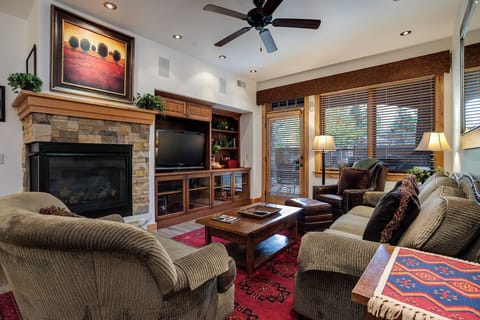 Unwind in your cozy living room featuring a warm stone fireplace, plush seating, and natural light filtering through wooden blinds—perfect for relaxing evenings after mountain adventures.