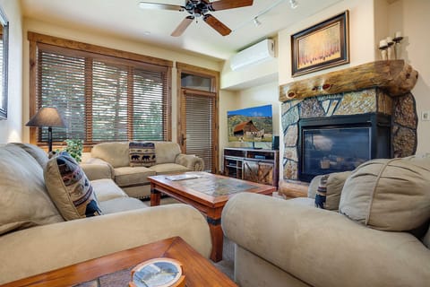 Sink into these plush sofas beside the stone fireplace, where rustic wood beams meet mountain charm. Your cozy mountain retreat awaits with comfortable seating and natural light streaming through wooden blinds.
