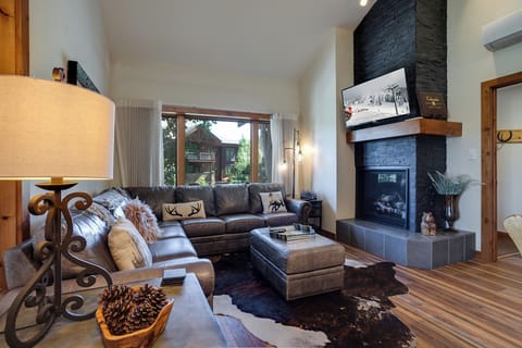 Relax in your inviting living space, where a cozy fireplace, plush leather seating, and mountain views through large windows create the perfect retreat after a day of adventure.