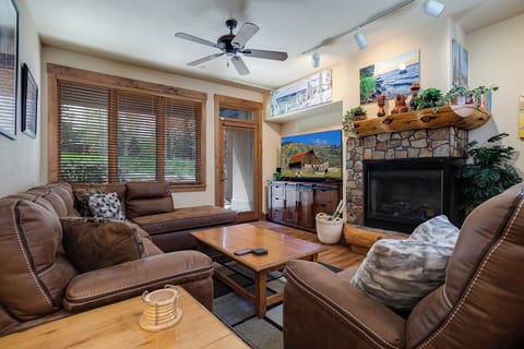 Unwind in your cozy living room with plush leather seating, a warm stone fireplace, and natural light streaming through wooden blinds—your perfect retreat after a day of adventure.