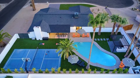 Resort-style backyard featuring a private pool, poolside loungers, a multi-sport court for basketball, pickleball, and tennis, turf with cornhole, a pergola with a built-in BBQ and bar seating, and a covered patio with outdoor dining table for 10. 