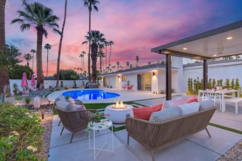 Relaxing backyard oasis featuring a fire pit, comfortable lounge seating, a covered cabana, a pristine pool, and a custom water feature.