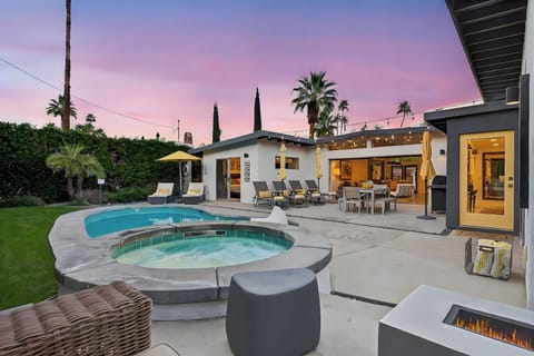 Modern outdoor paradise with sparkling pool, hot tub, and cozy fire pit under a stunning sunset sky.