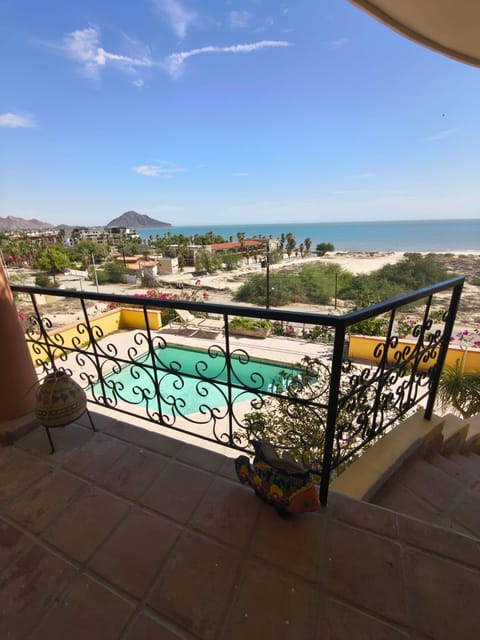 A sweeping aerial view from the wrought iron balcony railing overlooking the private pool, sandy coastline, and distant mountains of the Sea of Cortez.