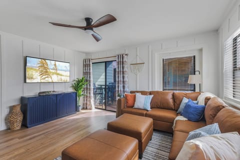 Bright coastal living room with leather sectional, TV, and private balcony access