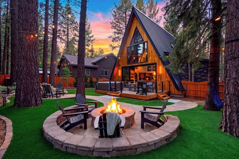 Twilight firepit vibes with Adirondack seating, forest views, and the glowing A-frame setting the scene for relaxed mountain evenings.