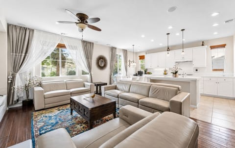 Bright living room with cozy seating, big windows, and an open kitchen nearby.