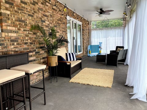 Settle into the covered sunroom, where cushioned seating, glowing string lights, a ceiling fan, and backyard views create your breezy hangout spot ✨
