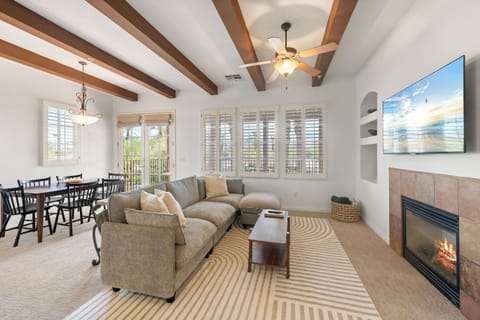Bright living room with fireplace, TV, dining area, and vaulted beam ceilings