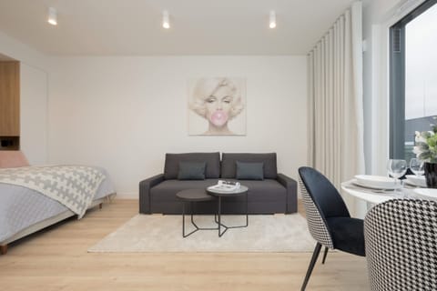 A cozy studio setup with a gray sofa, a small round dining table, and a prominent Marilyn Monroe portrait on the wall, creating a modern yet playful vibe.

