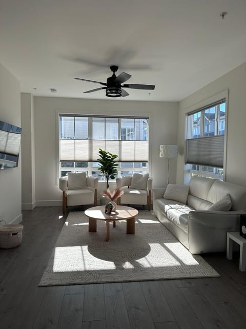 Living room with white leather sofa, two cushioned armchairs, round wooden coffee table, and dark wood flooring.